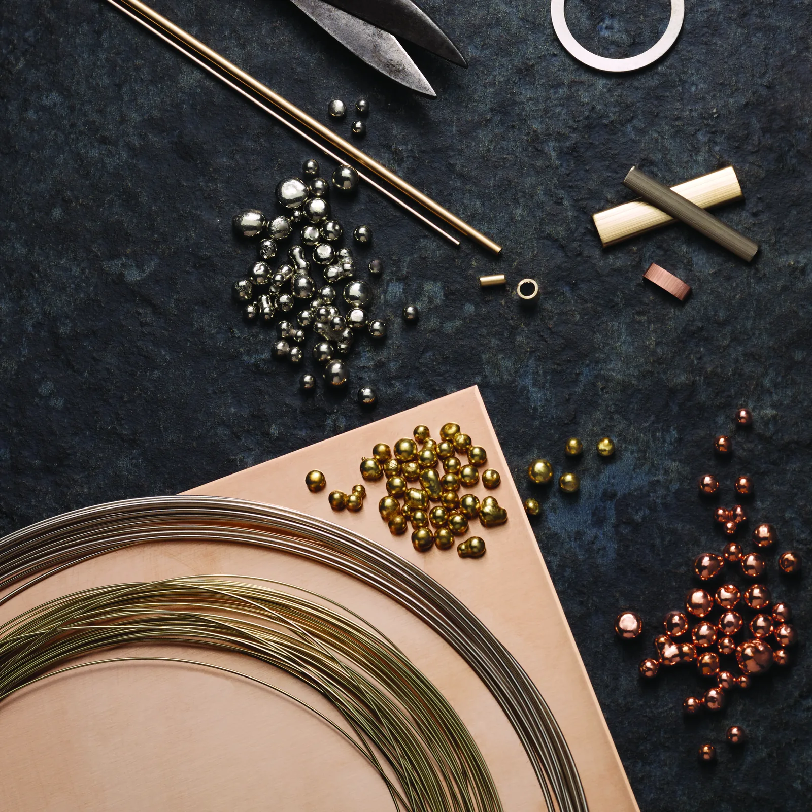 Silver, gold, and copper alloy components arranged on a jeweler's work surface